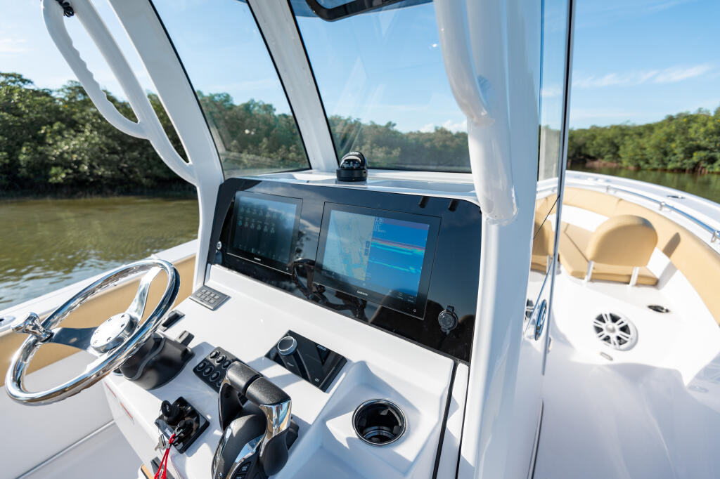Helm station with dual touchscreen displays, steering wheel, and control console overlooking a mangrove-lined river