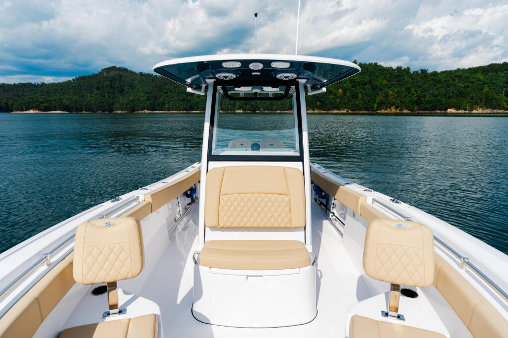 Center console boat with cream-colored seating and hard top, anchored in calm lake waters with forested shoreline behind