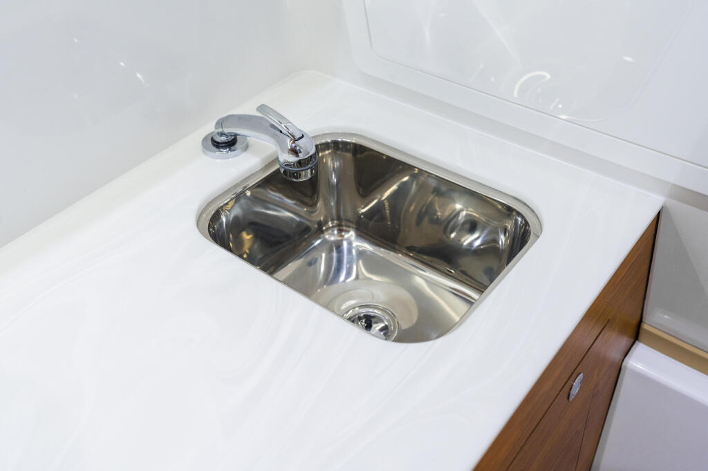 Stainless steel dual-basin sink with chrome faucet mounted on white countertop with wood cabinetry