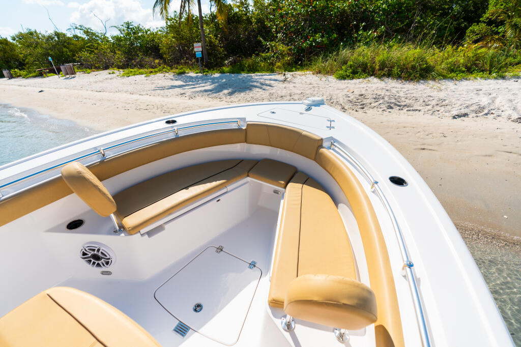 Bow seating area of center console boat with tan upholstery beached on sandy shore