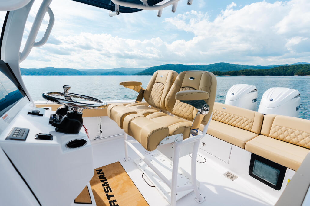 Helm station and tan leather seating on a center console boat with calm lake and forested mountains in background