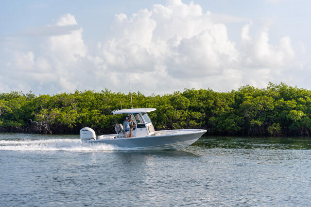 White center console boat running through shallow mangrove-lined waters with two people at the helm