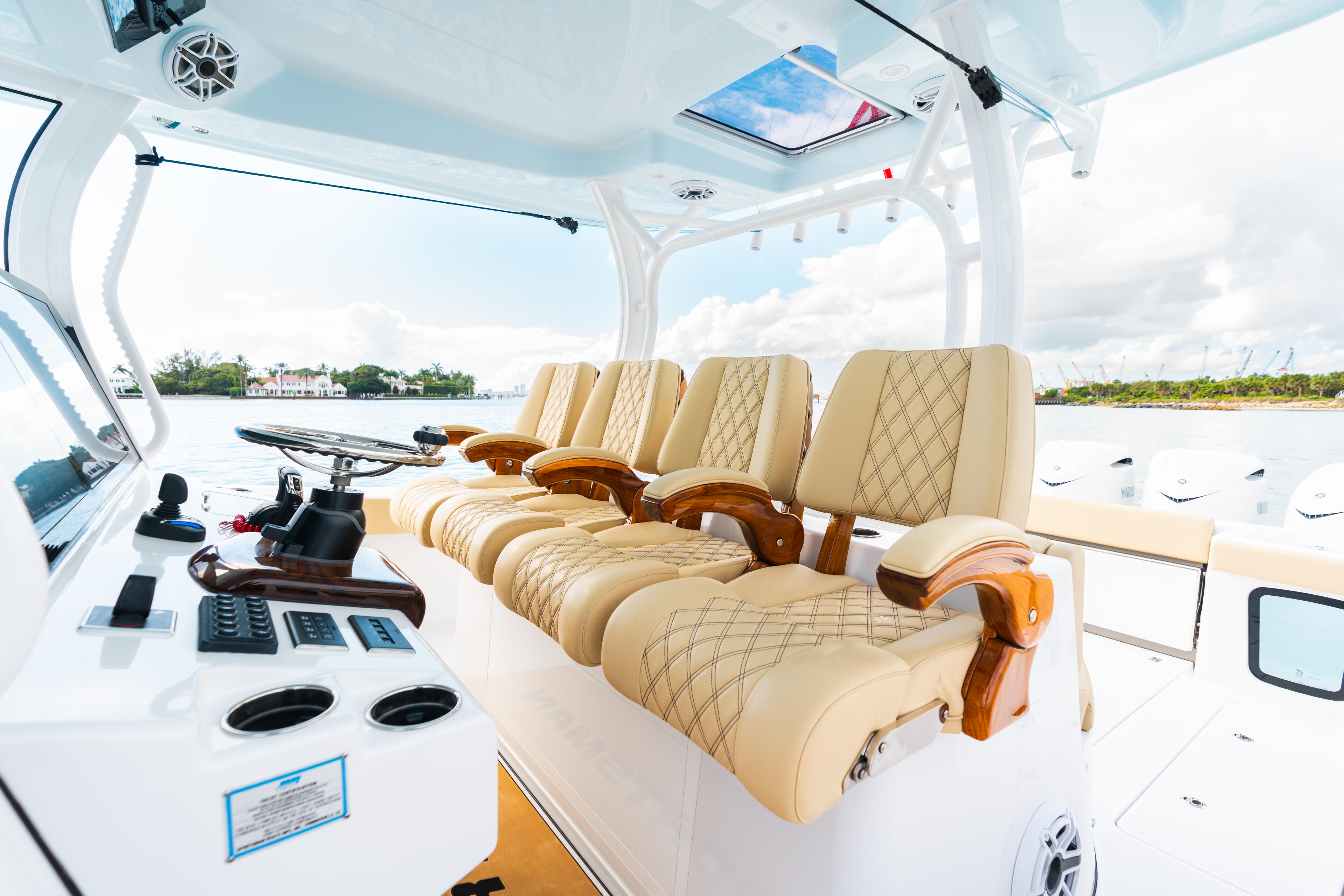 Open center console boat with quad captain's chairs, helm electronics, and waterfront view under hard-top canopy