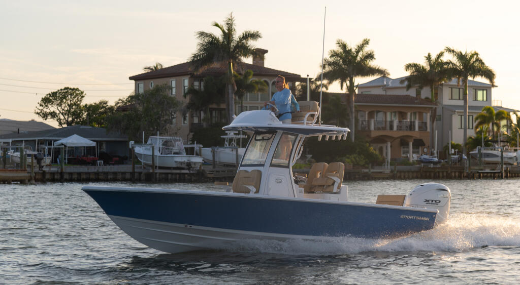 Blue and white center console boat running through shallow water with waterfront homes and palm trees in background