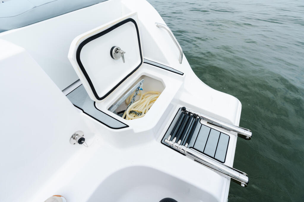 Overhead view of boat deck showing open storage hatch with coiled rope, switch panel, and calm green water
