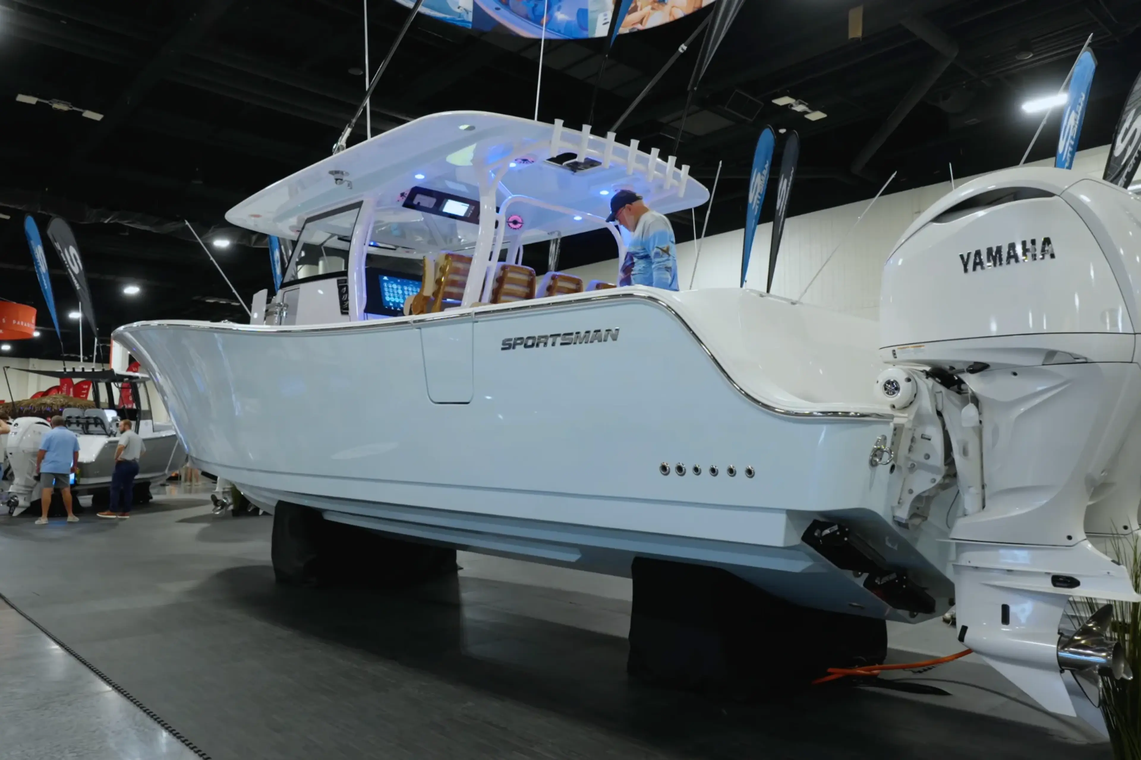 White Sportsman boat with hard-top displayed at indoor marina show next to Yamaha outboard motor