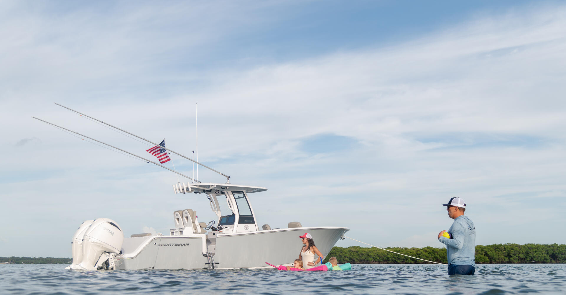 Family swimming and wading near a white center console boat anchored at a sandbar with fishing rods deployed