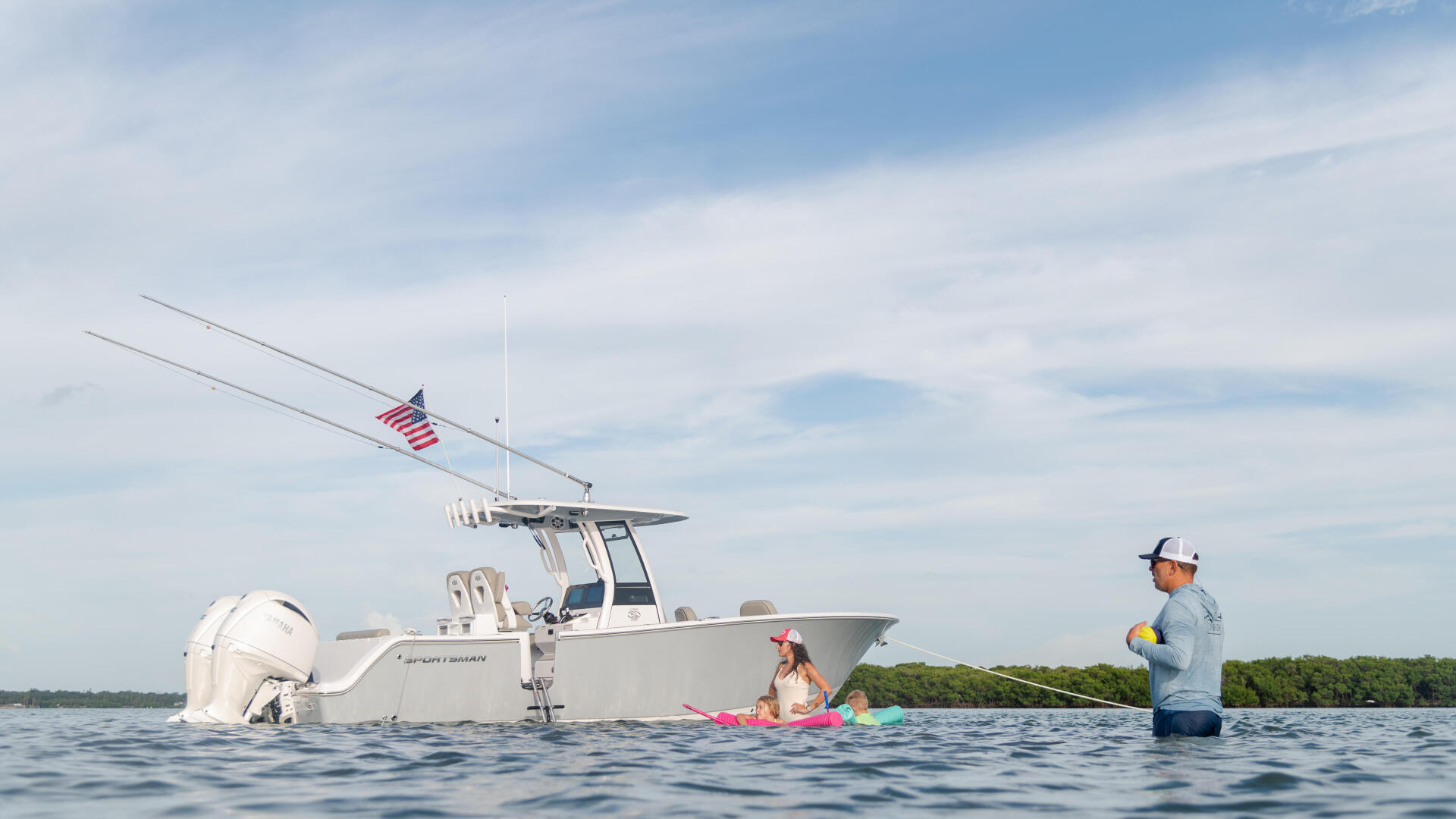Family swimming and wading near a white center console boat anchored at a sandbar with fishing rods deployed