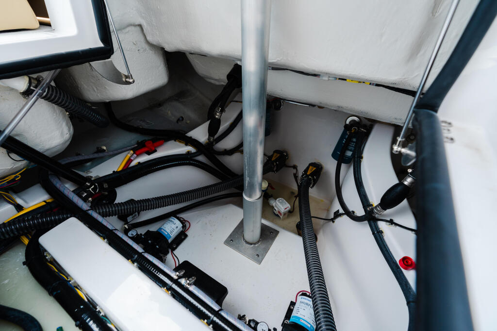Boat engine compartment showing wiring, hoses, and electrical components organized beneath cushioned storage areas