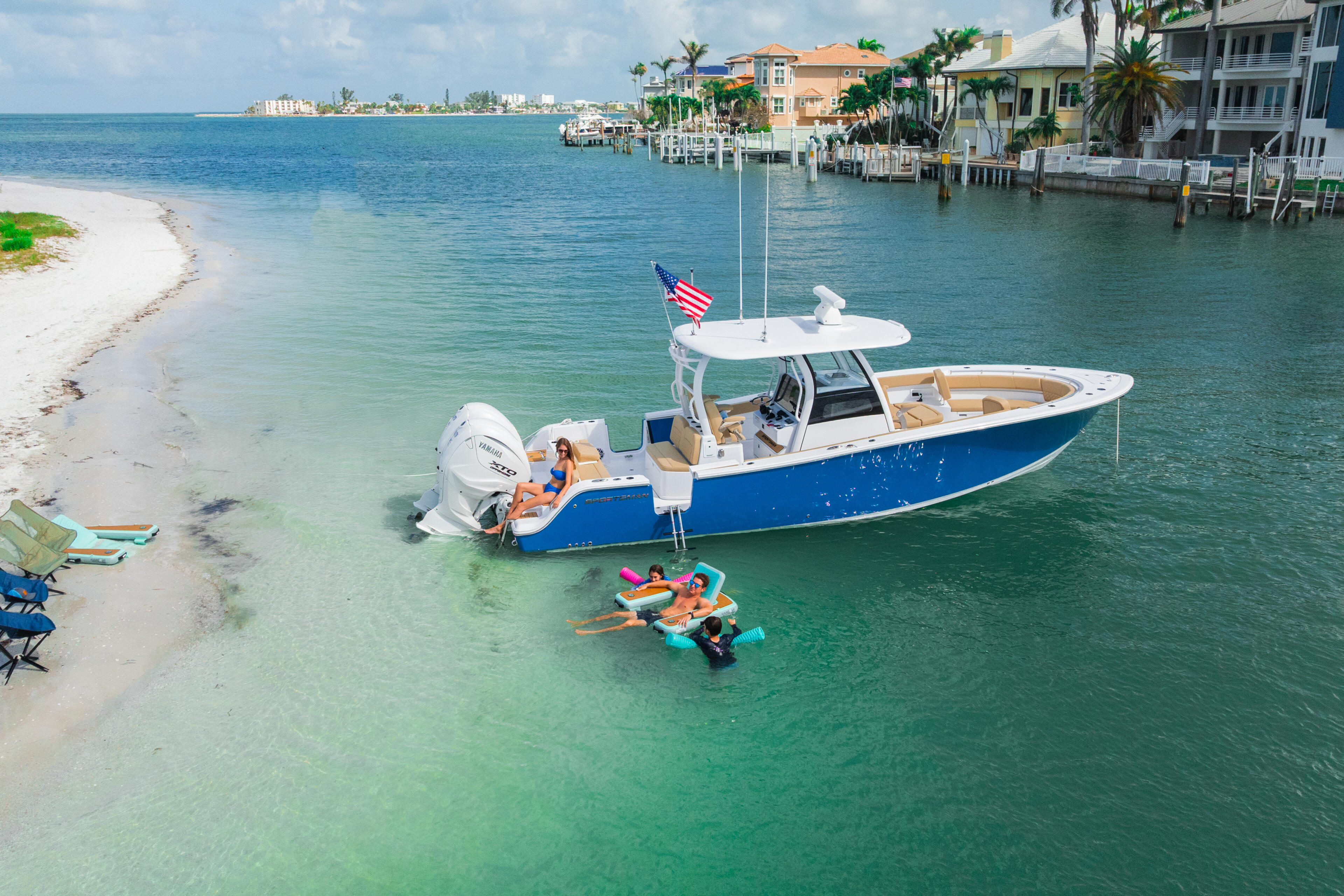 Blue and white center console boat anchored in shallow turquoise water with family swimming and relaxing on nearby beach