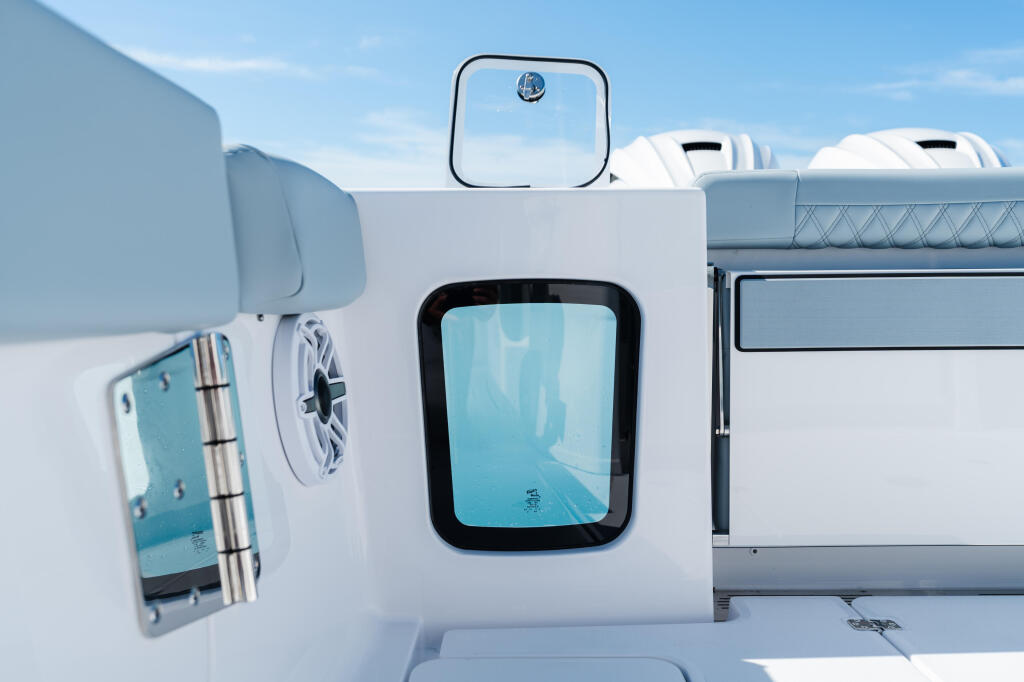 Cabin exterior of boat showing window, ventilation fan, mirror and railing details against blue sky