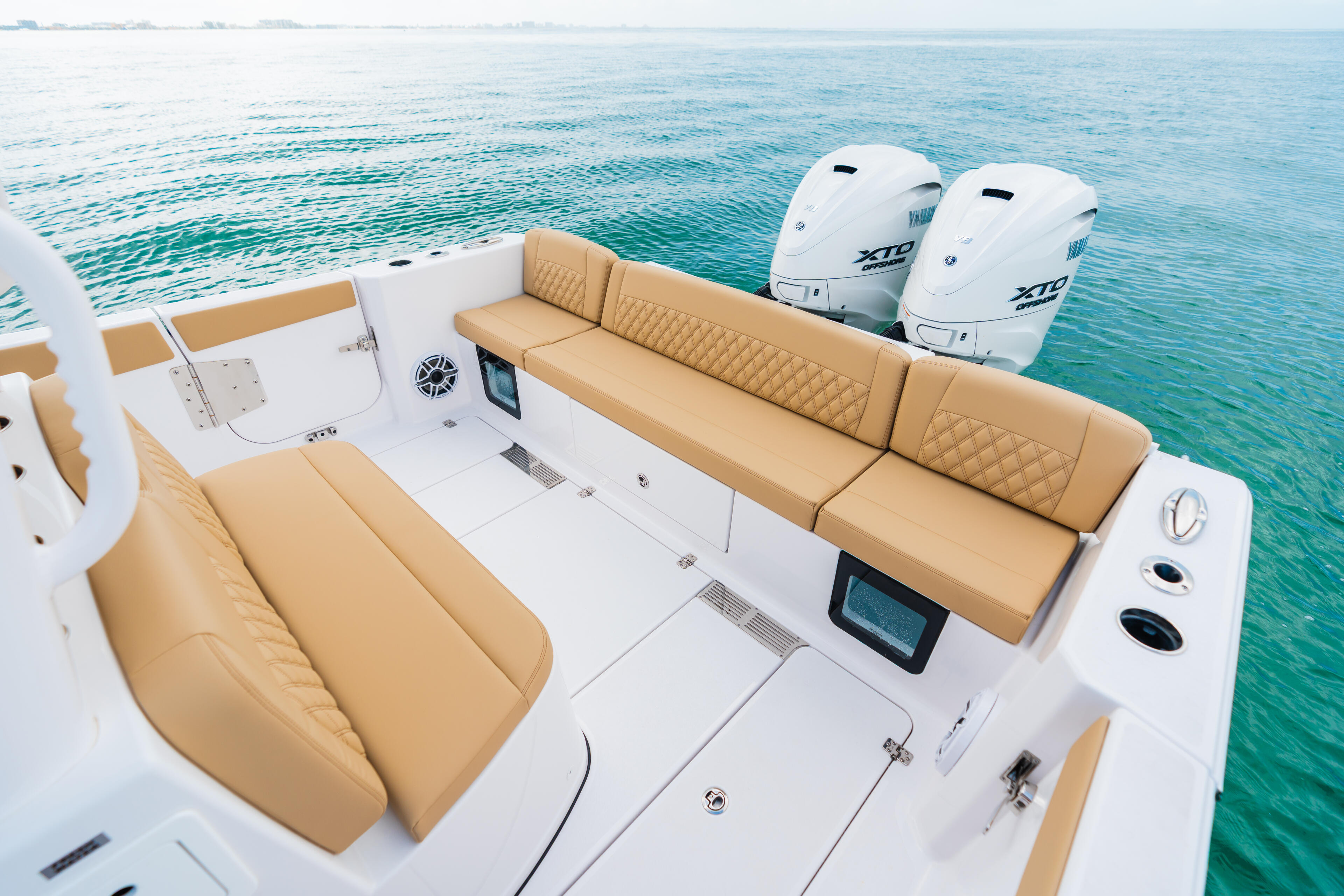Aerial view of boat's seating area with tan cushioned loungers, white deck, dual outboard engines, and calm turquoise water
