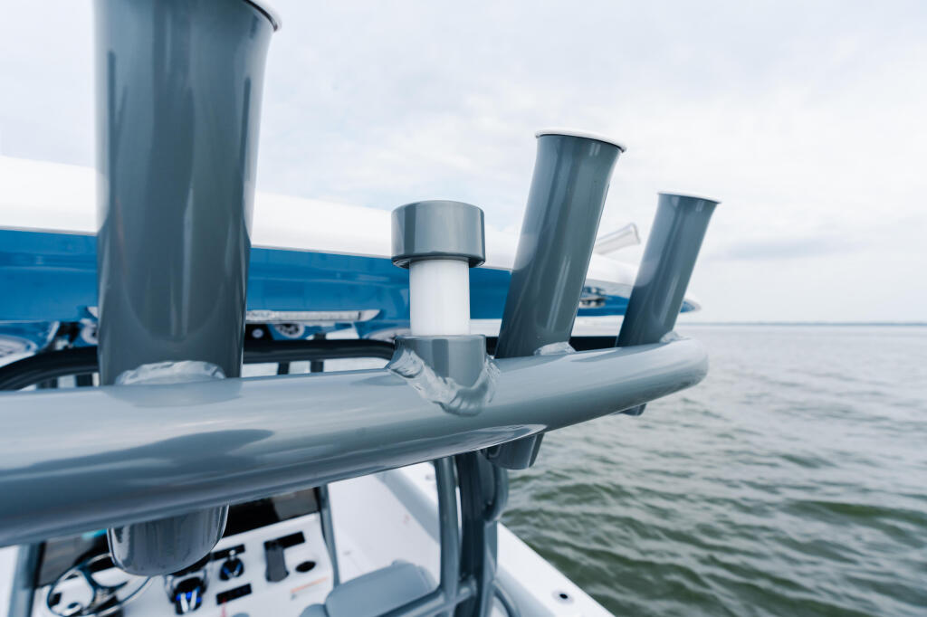 Close-up of boat's gray powder-coated railing and rod holders with calm water and marina in background