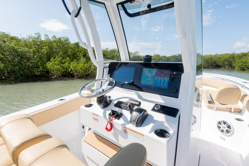 Helm console with Garmin GPS display, steering wheel, and control panels overlooking mangrove shoreline