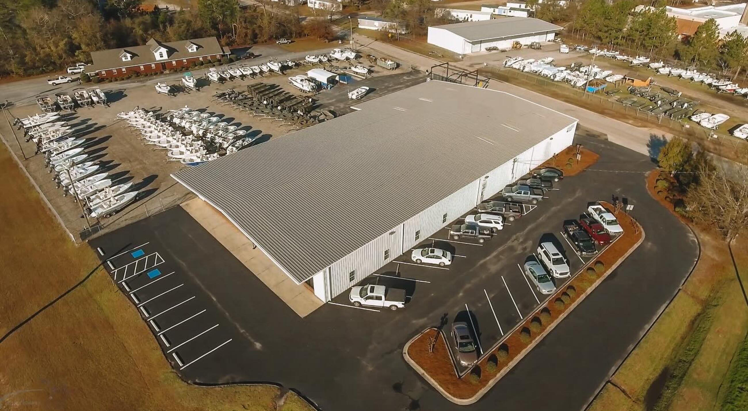 Aerial view of a marine dealership with hundreds of boats displayed in organized rows and a large warehouse facility with parking lot
