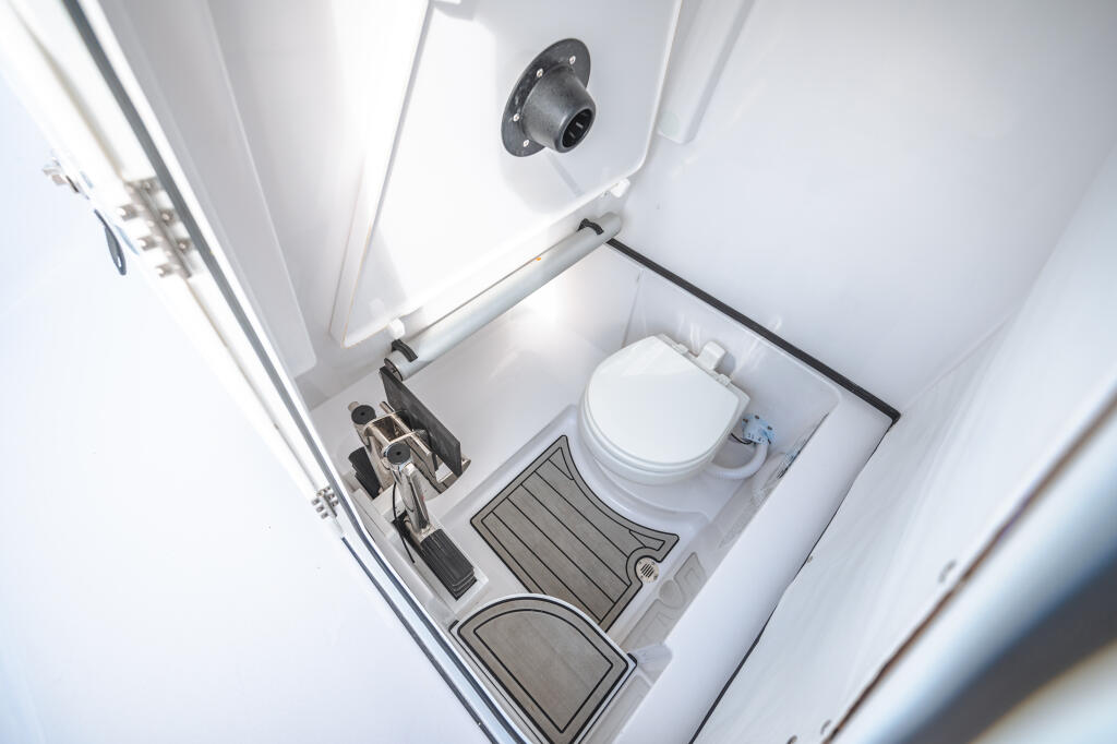 Overhead view of a boat cabin head with electric porcelain toilet, ventilation, and compact storage compartments