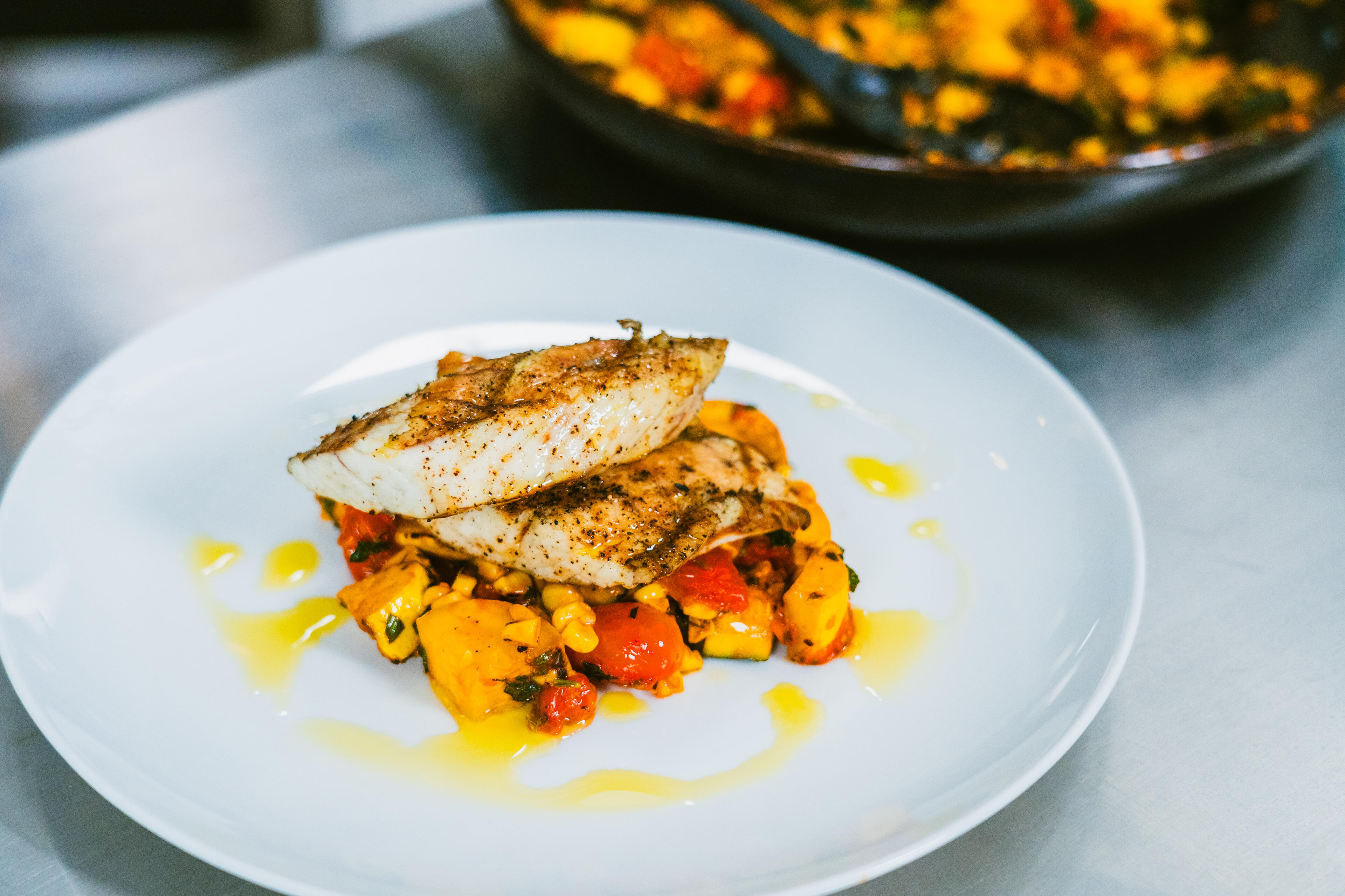 Seared redfish fillet with herb crust served over roasted vegetables and drizzled with oil