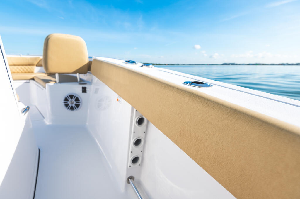 Tan bolstered helm seat and starboard gunwale on a white center console boat in calm blue water