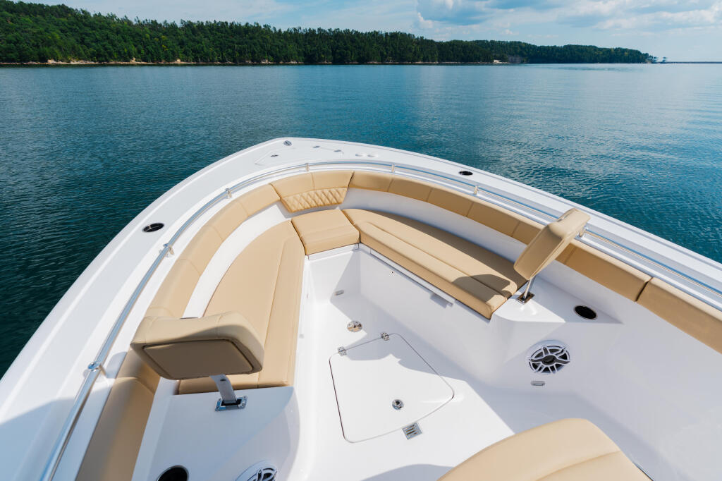 Bow seating area of a white and tan center console boat on calm blue water with forested shoreline in background