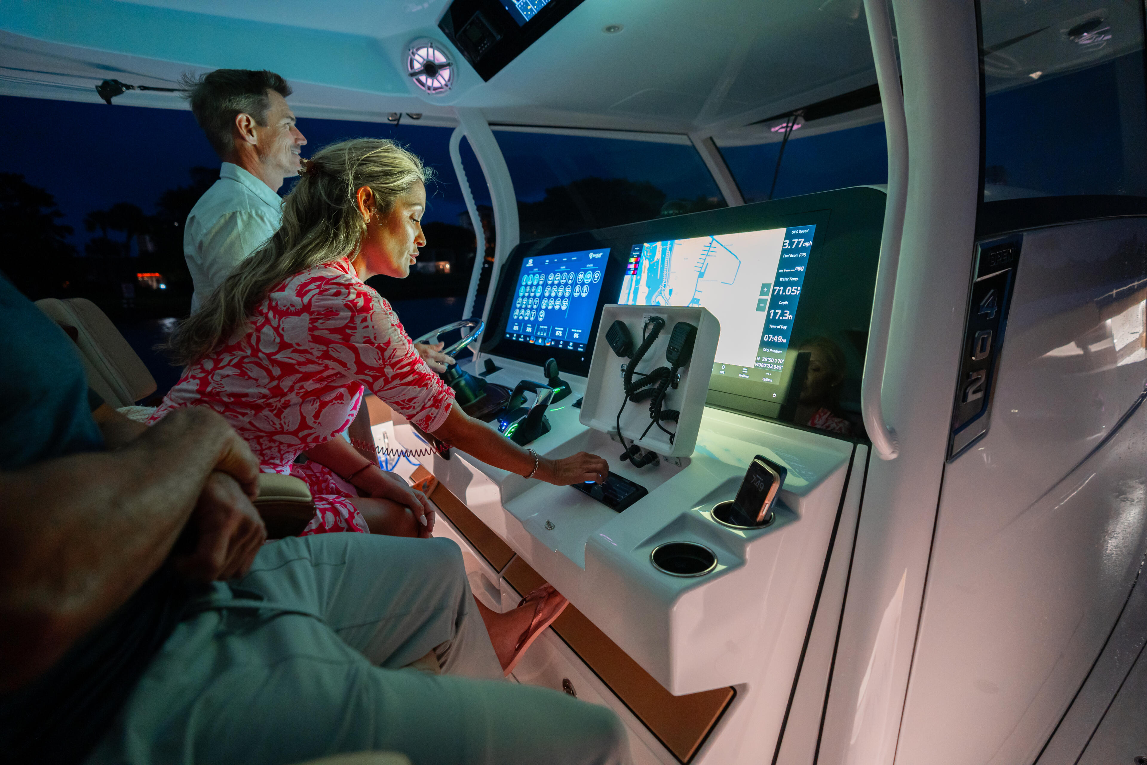 Couple at the helm of a boat with navigational displays and controls illuminated at dusk