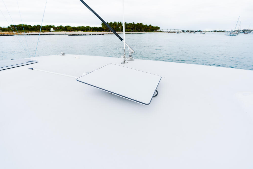 Clean white boat deck with cushioned seating area overlooking a calm marina with sailboats and tropical shoreline