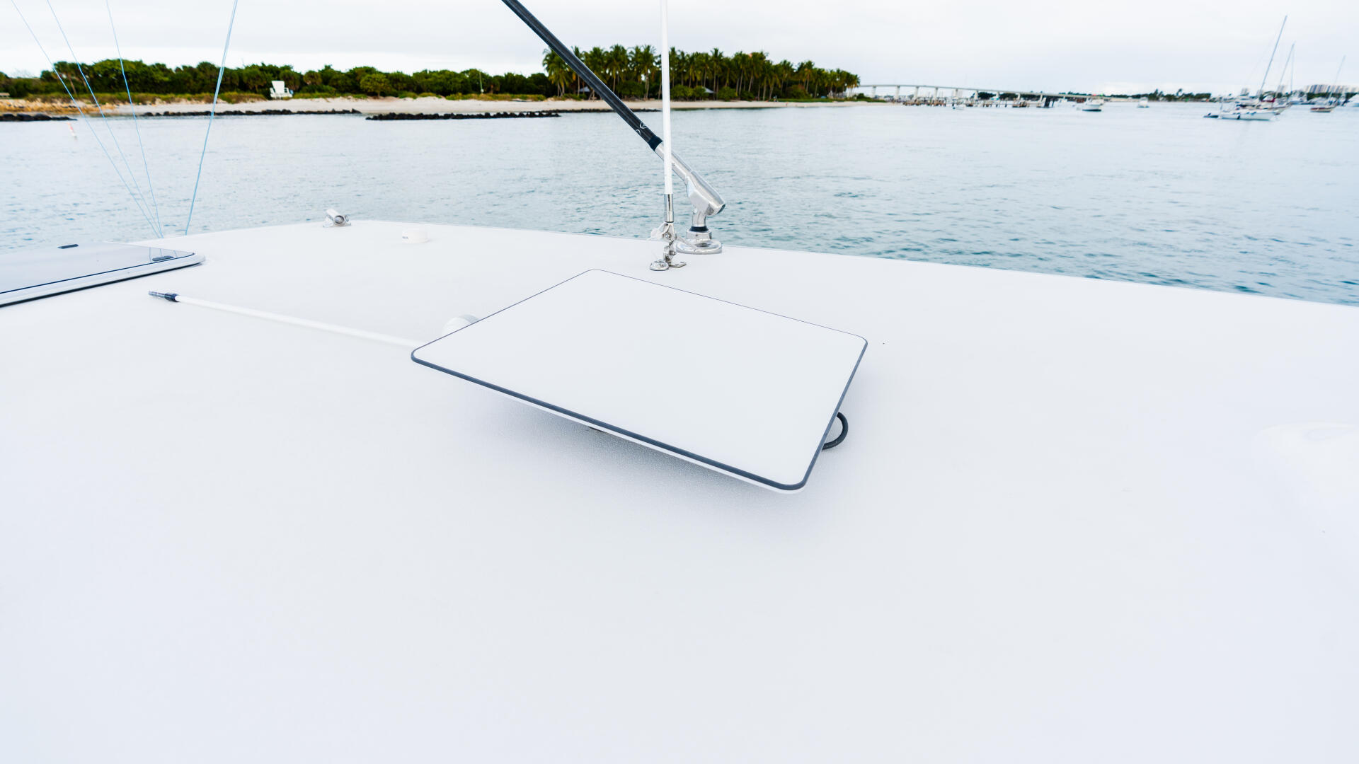 Clean white boat deck with cushioned seating area overlooking a calm marina with sailboats and tropical shoreline