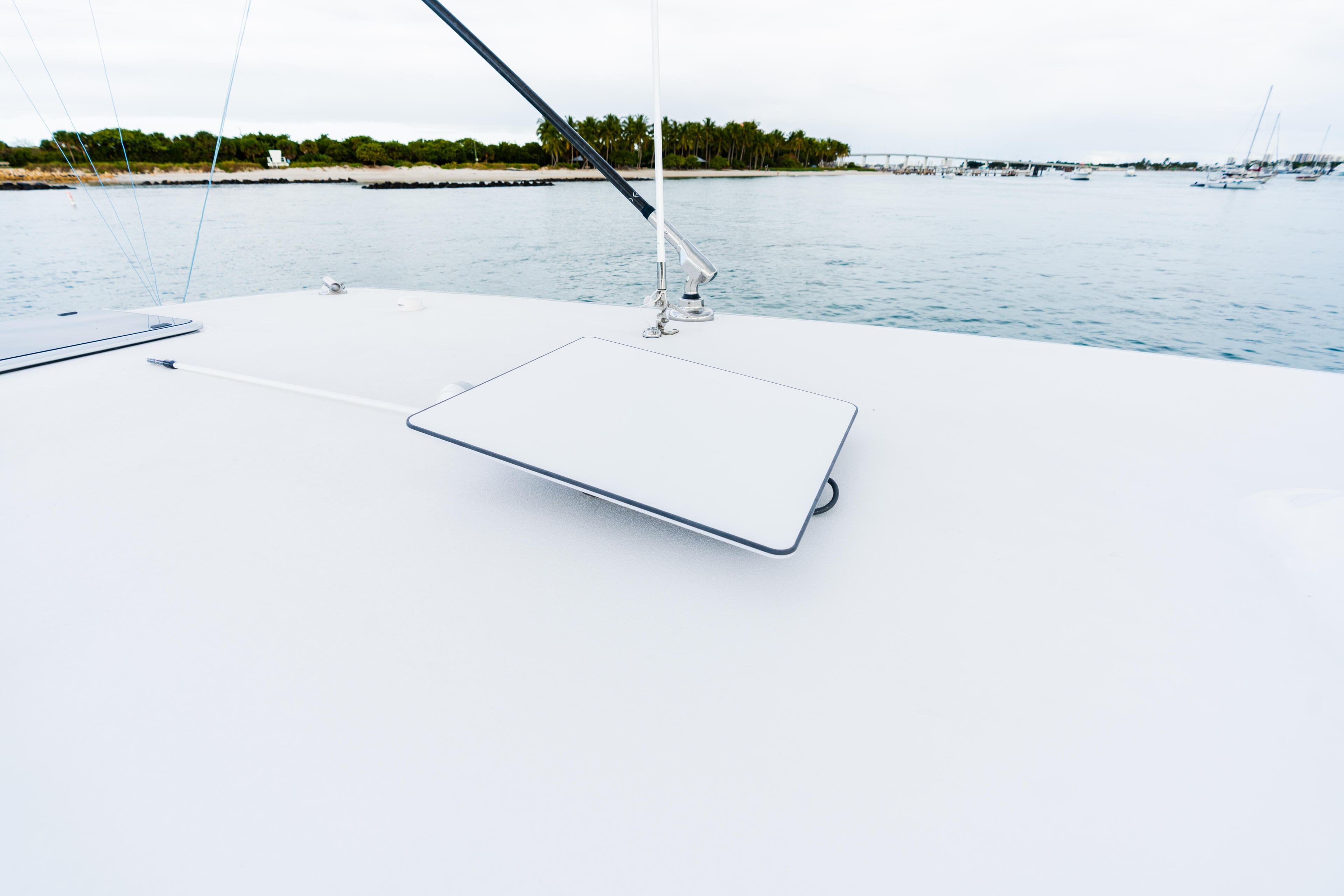 Clean white boat deck with cushioned seating area overlooking a calm marina with sailboats and tropical shoreline