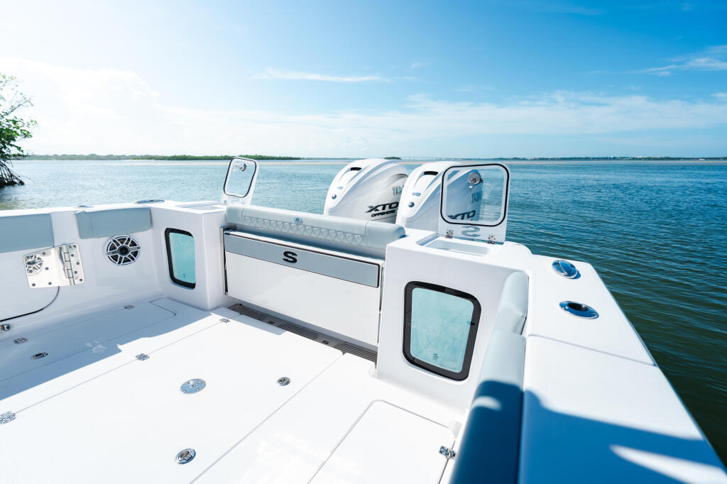 Open 322 center console boat with white deck, storage hatches, and windshield anchored in calm blue water