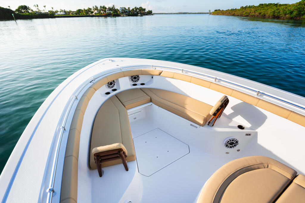 Bow seating area of a center console boat with tan cushions overlooking calm blue water and mangrove shoreline