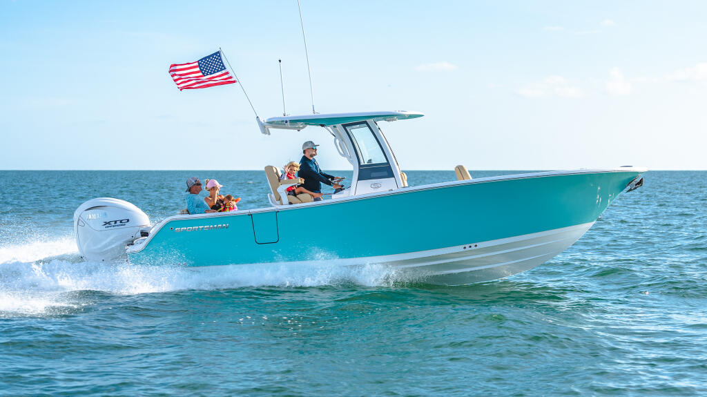 Turquoise center console boat running through shallow water with family aboard, American flag flying from hard-top
