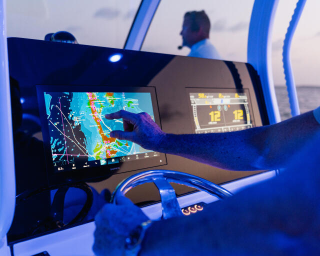 Captain points to fish on colorful sonar display at helm during offshore cruise