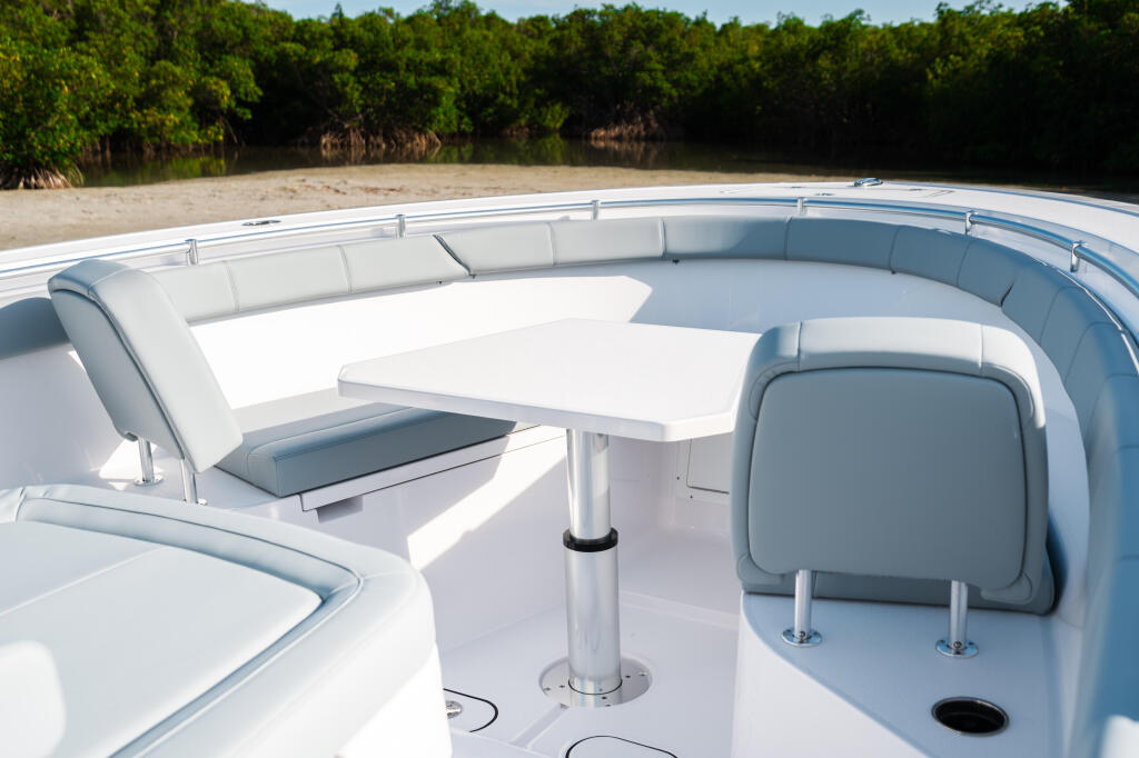 Open 322 boat's sun-filled cockpit with white seating, table, and mangrove shoreline backdrop