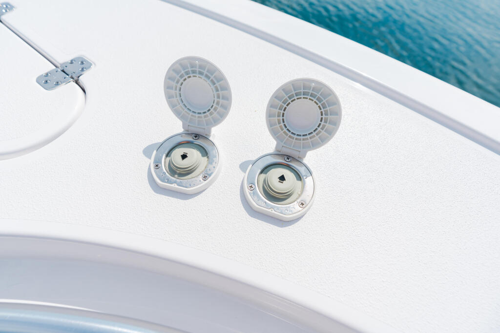 Two white ventilation fans with circular louvers mounted on a boat's hard-top above blue water