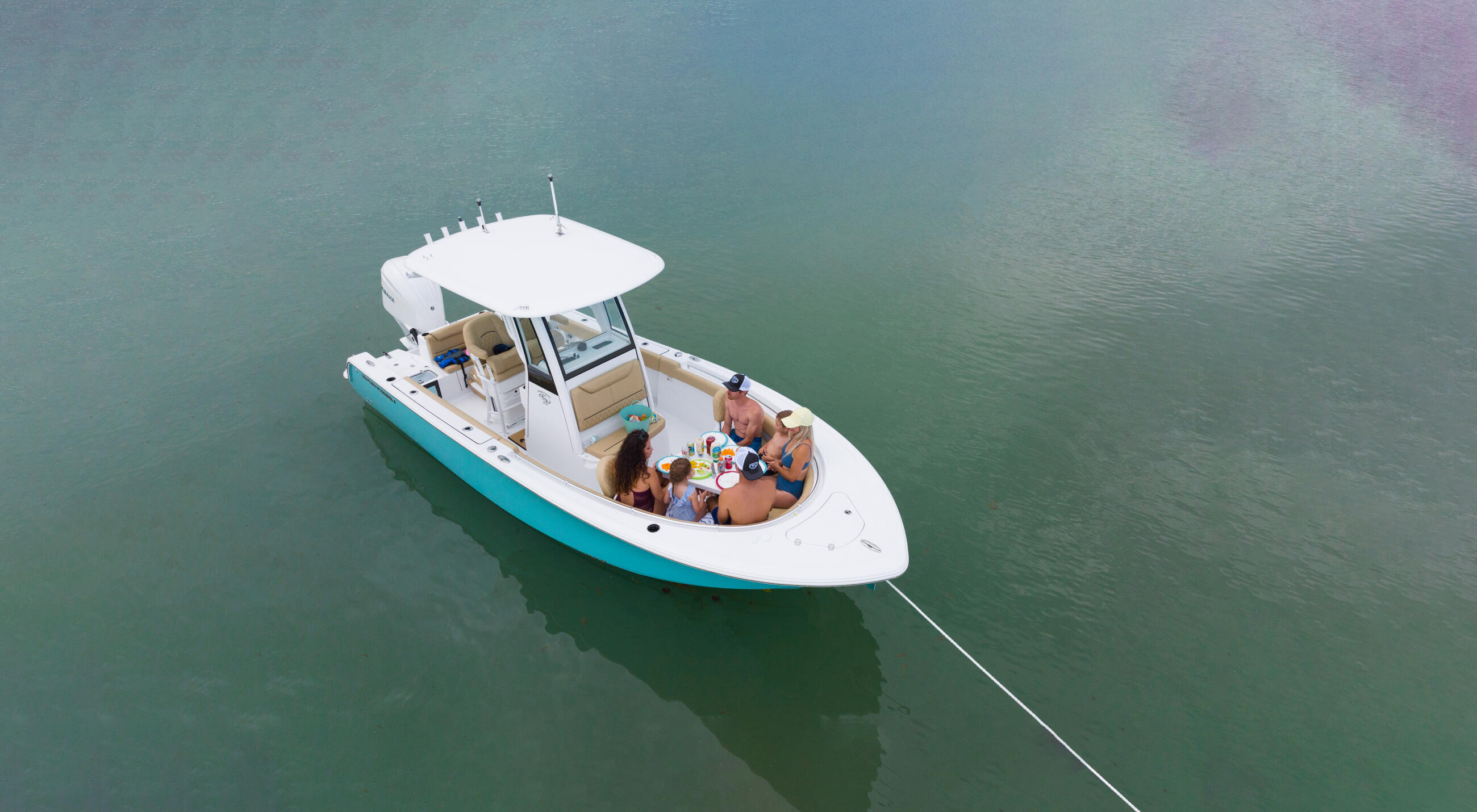 Family enjoying time together on a white and turquoise center console boat anchored in calm shallow water