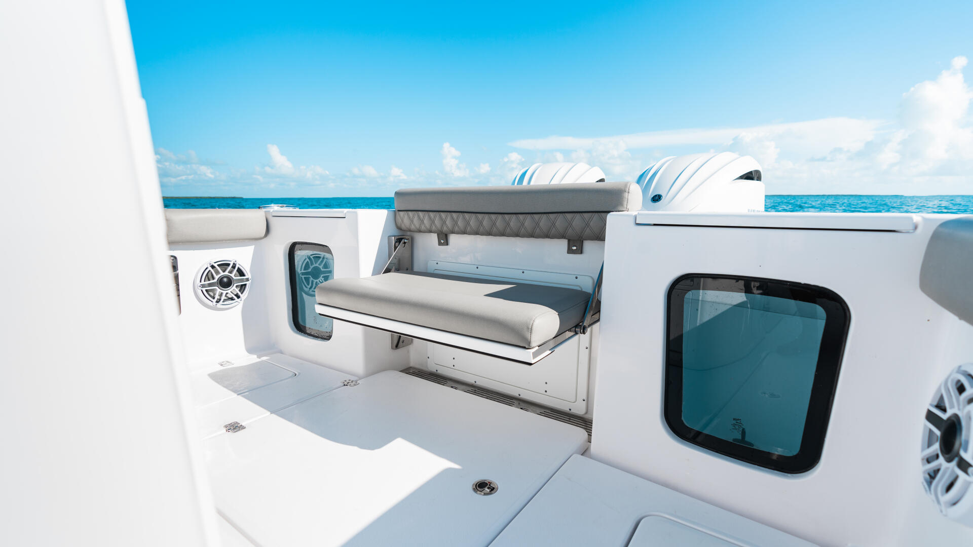 Open boat seating area with cushioned bench, storage compartments, and blue ocean vista in background