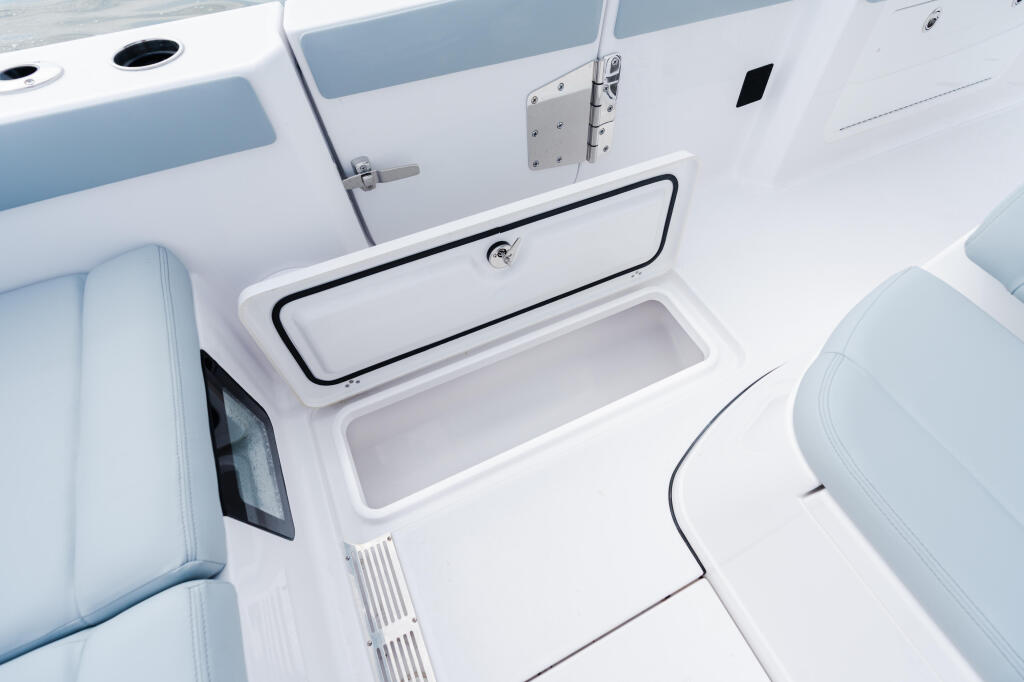 Open cooler storage compartment built into the boat's gunwale with black trim and drain plug