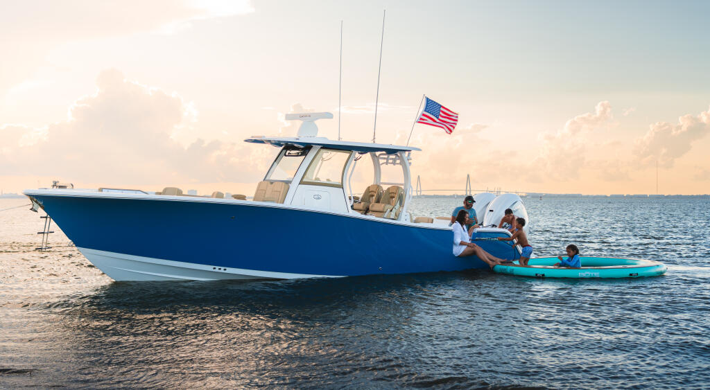 Family enjoying watersports from a blue and white fishing boat anchored at a sandy beach with kayaks in shallow water