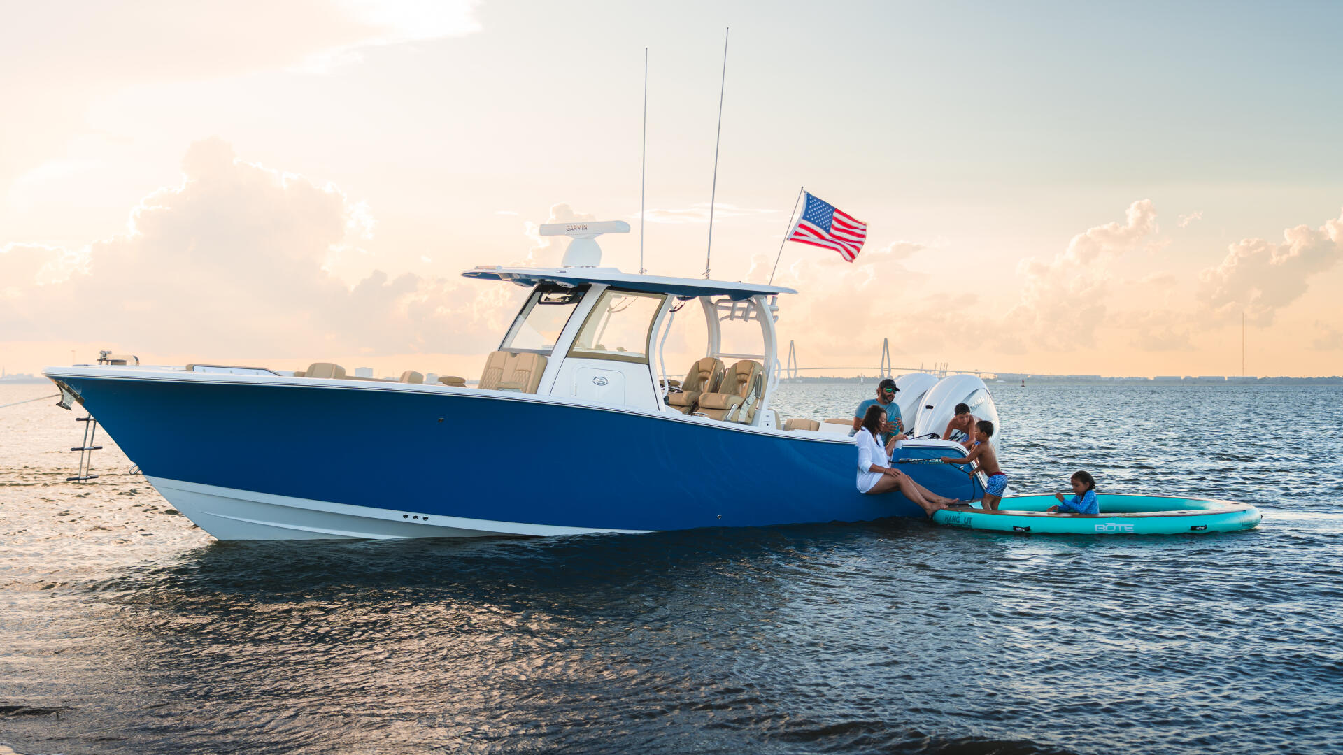 Family enjoying watersports from a blue and white fishing boat anchored at a sandy beach with kayaks in shallow water