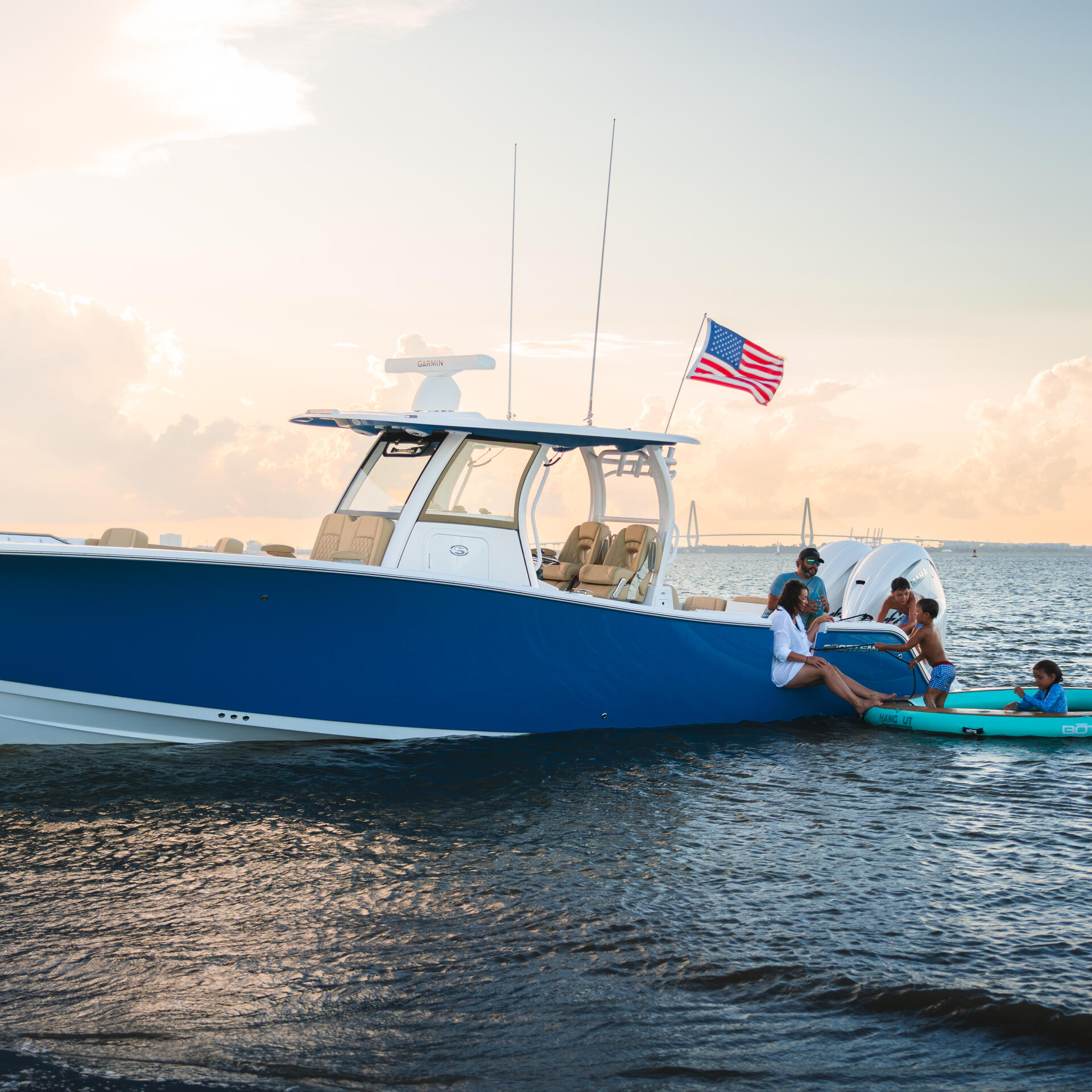Family enjoying watersports from a blue and white fishing boat anchored at a sandy beach with kayaks in shallow water