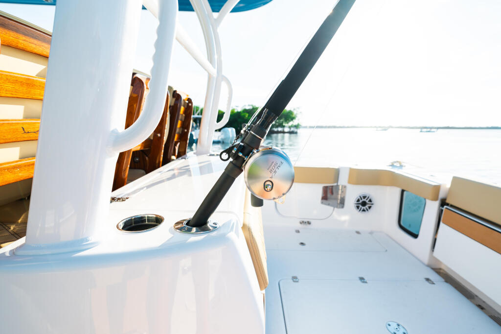 Fishing rod mounted on boat gunwale with calm water and distant shoreline visible