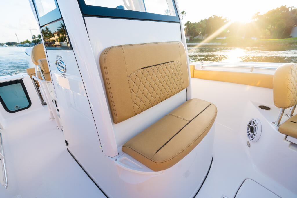 Tan quilted captain's seat and sunpad on white center console boat deck with water and palm trees at sunset
