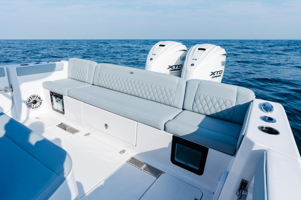 Spacious center console with gray quilted seating, dual outboard engines, and electronics mounted on starboard side, anchored offshore