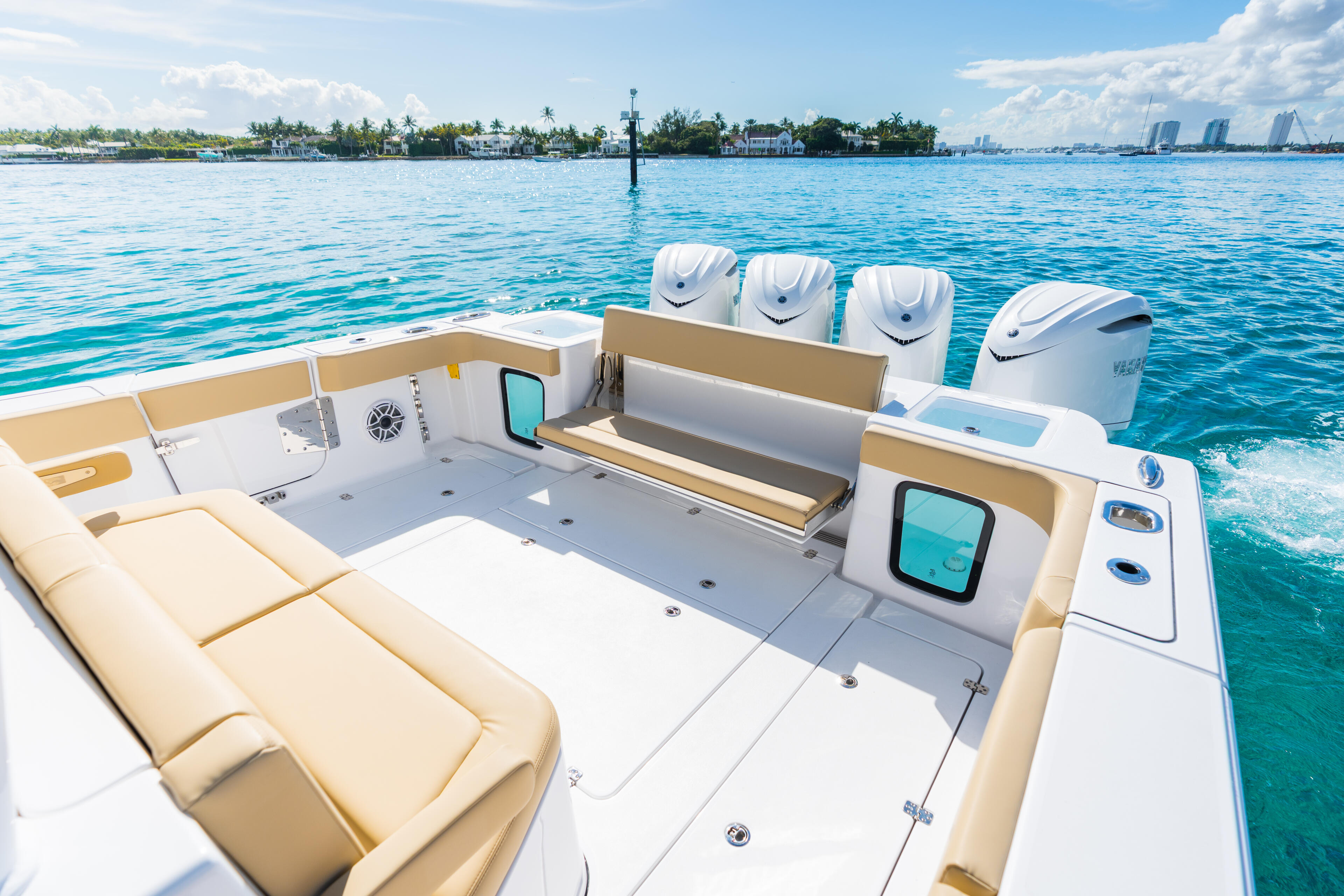 Open center console boat with cream seating, multiple outboard engines, and electronics overlooking waterfront homes and marina