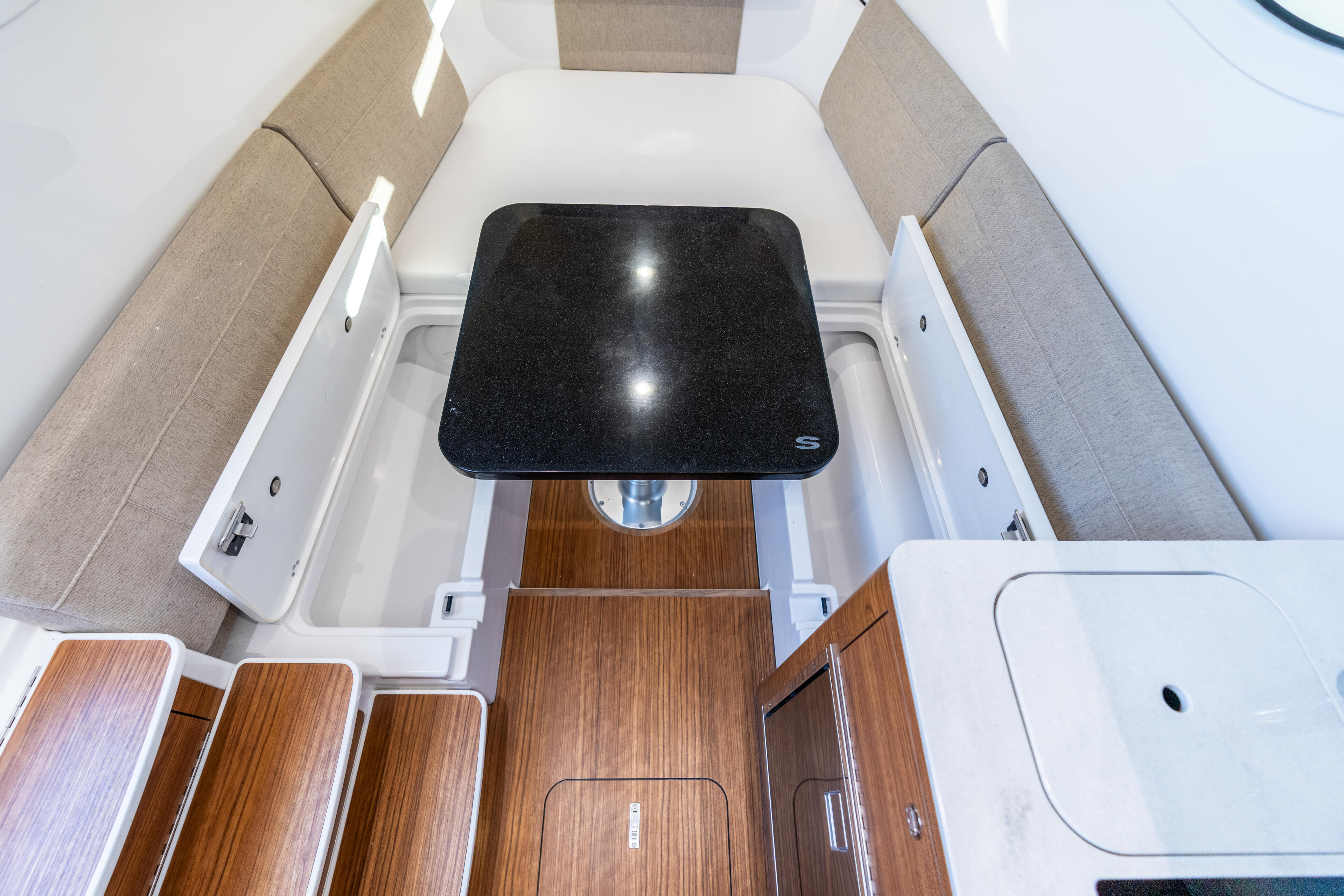 Overhead view of a boat cabin showing tan seating, wooden flooring, and a black dining table with LED lighting
