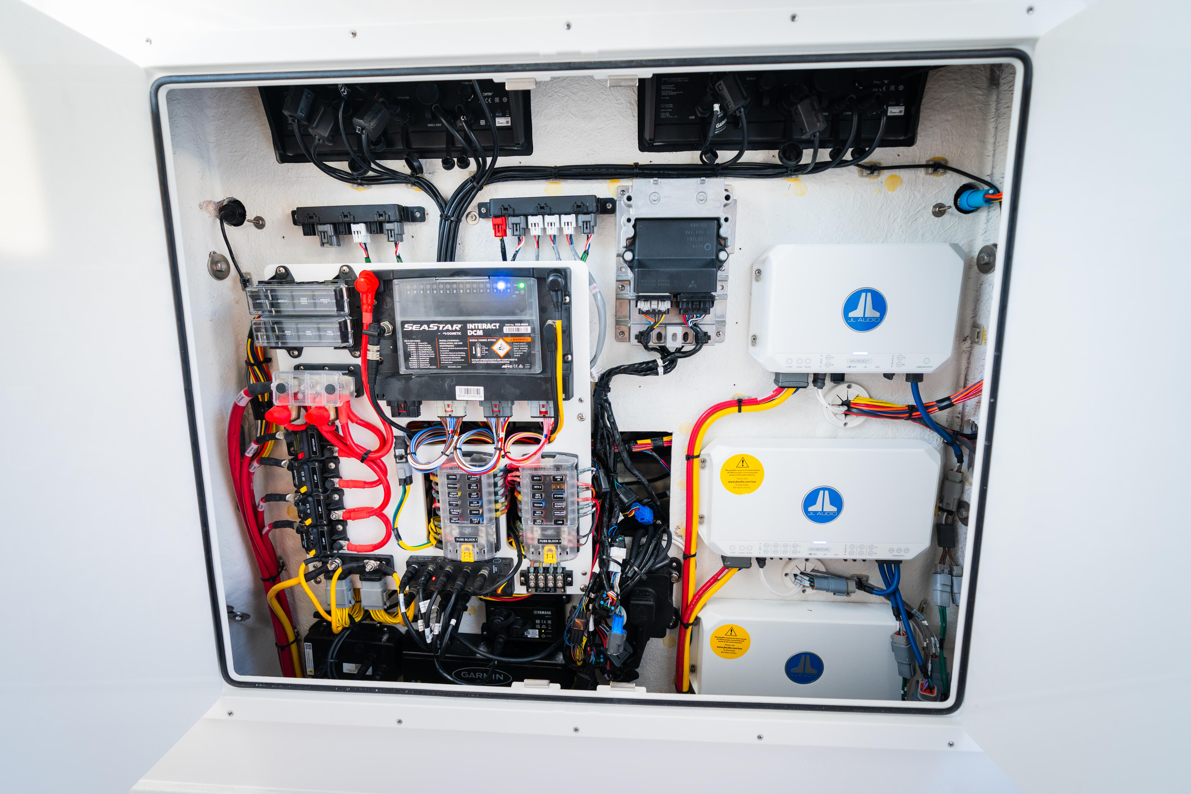 Open electrical panel showing fuse blocks, wiring, and JL Audio amplifiers with color-coded connections