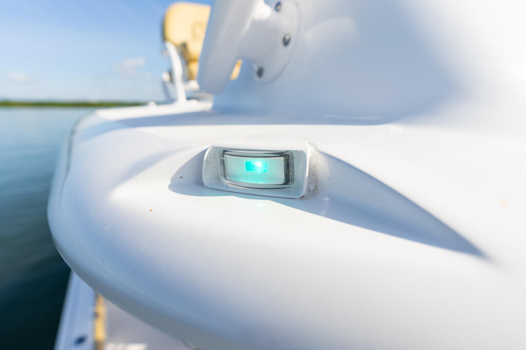 Green navigation light mounted on white boat hull with water and sky in background