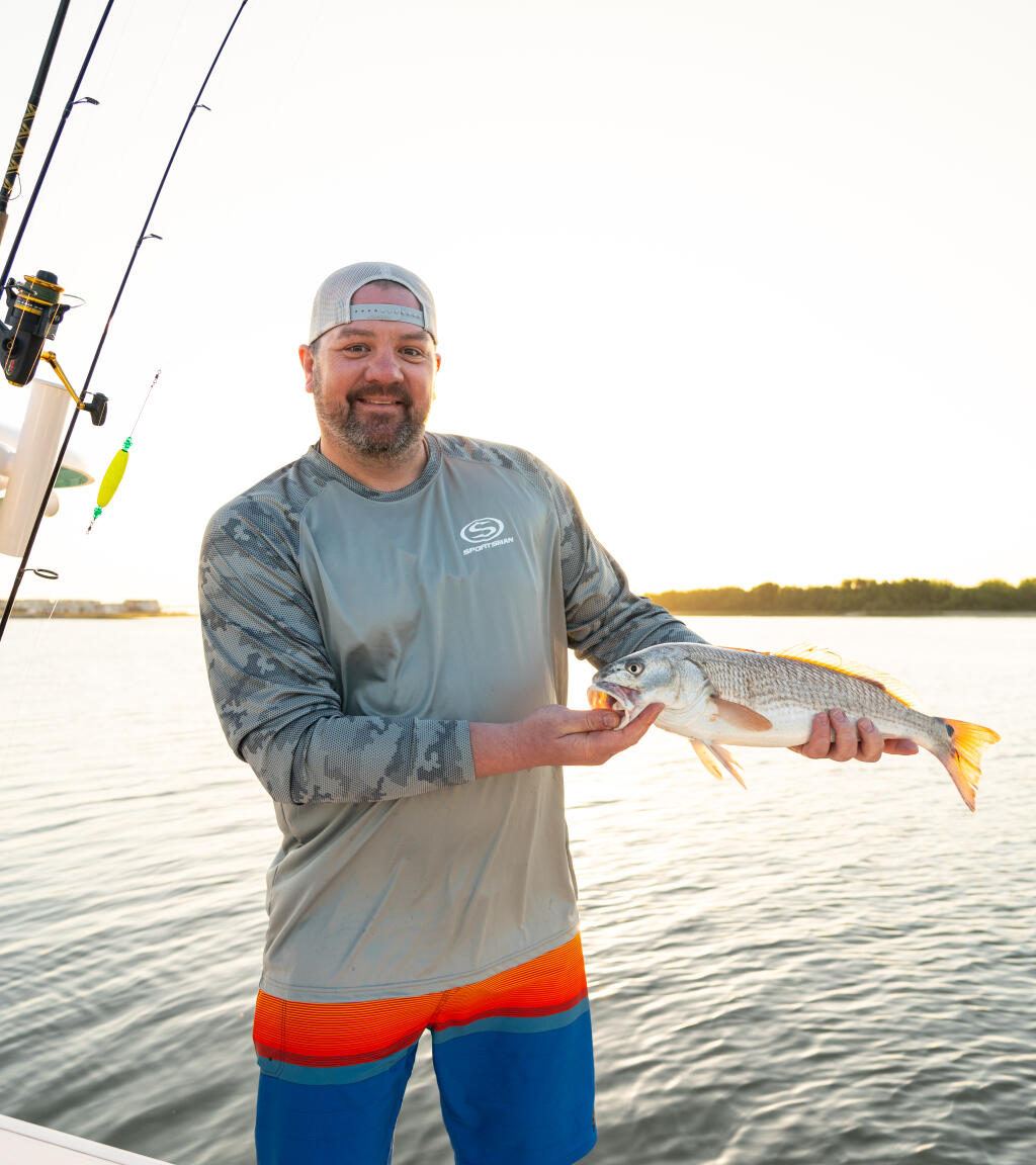 Angler holding a freshly caught redfish while standing on a boat with fishing rods visible in the background
