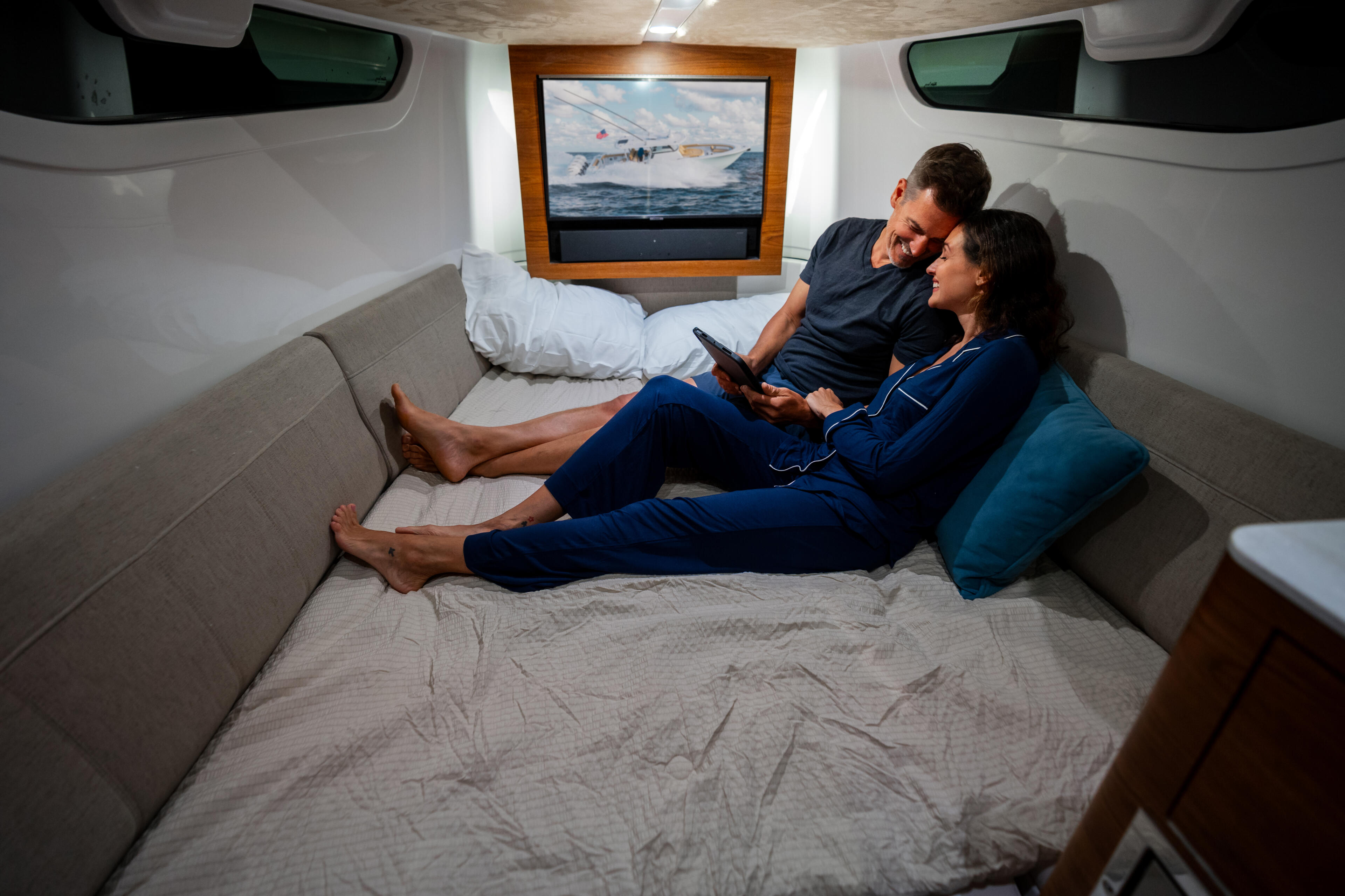 Couple relaxing in a boat's cabin berth with a flat-screen TV mounted on the wood-paneled wall