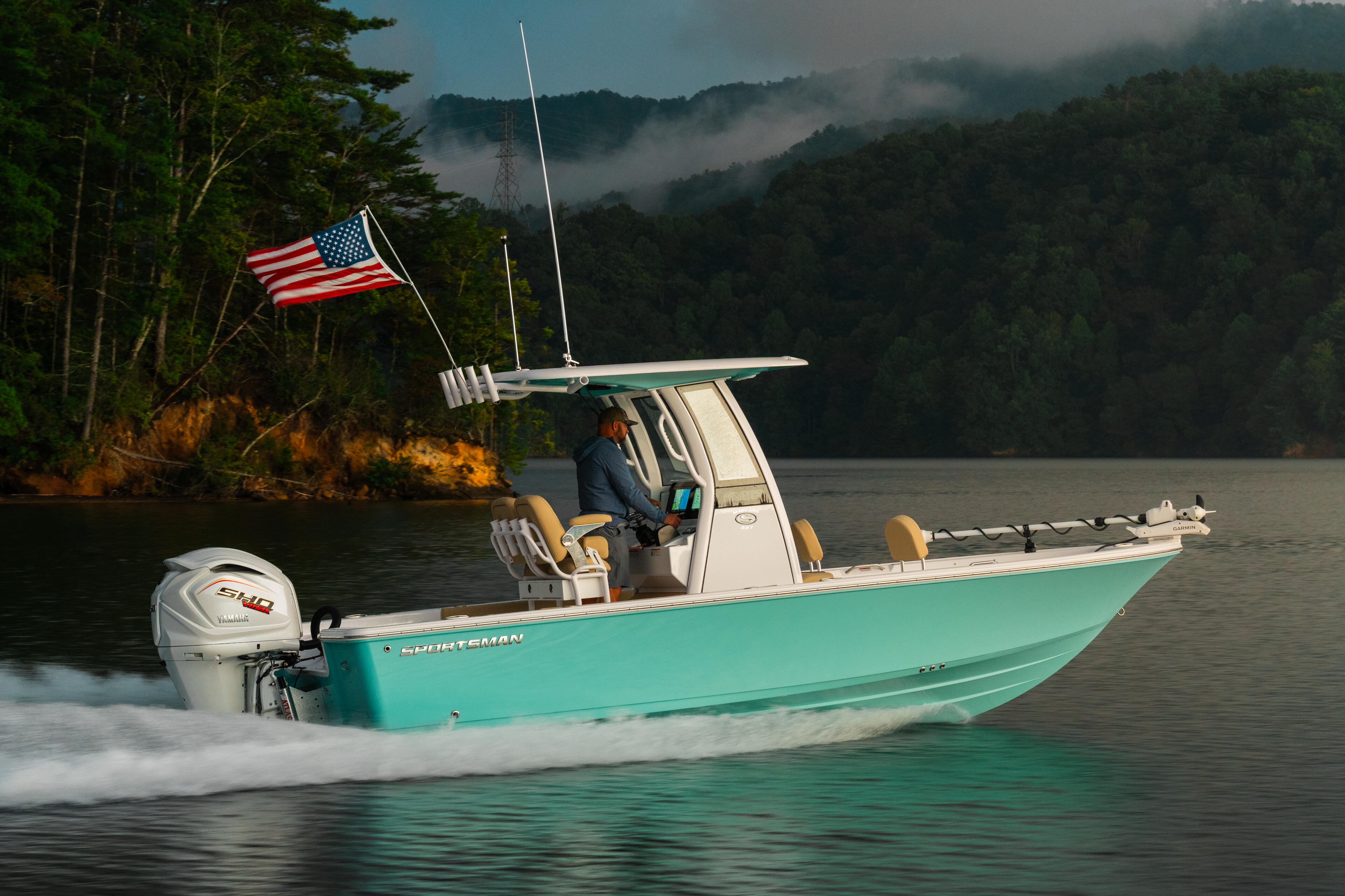 Turquoise fishing boat with hard-top running on misty mountain lake with American flag flying