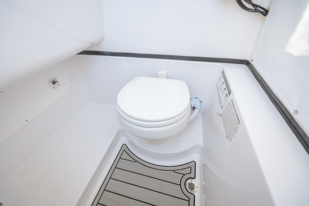 White electric marine toilet with closed lid installed in a compact cabin space with ventilation grill